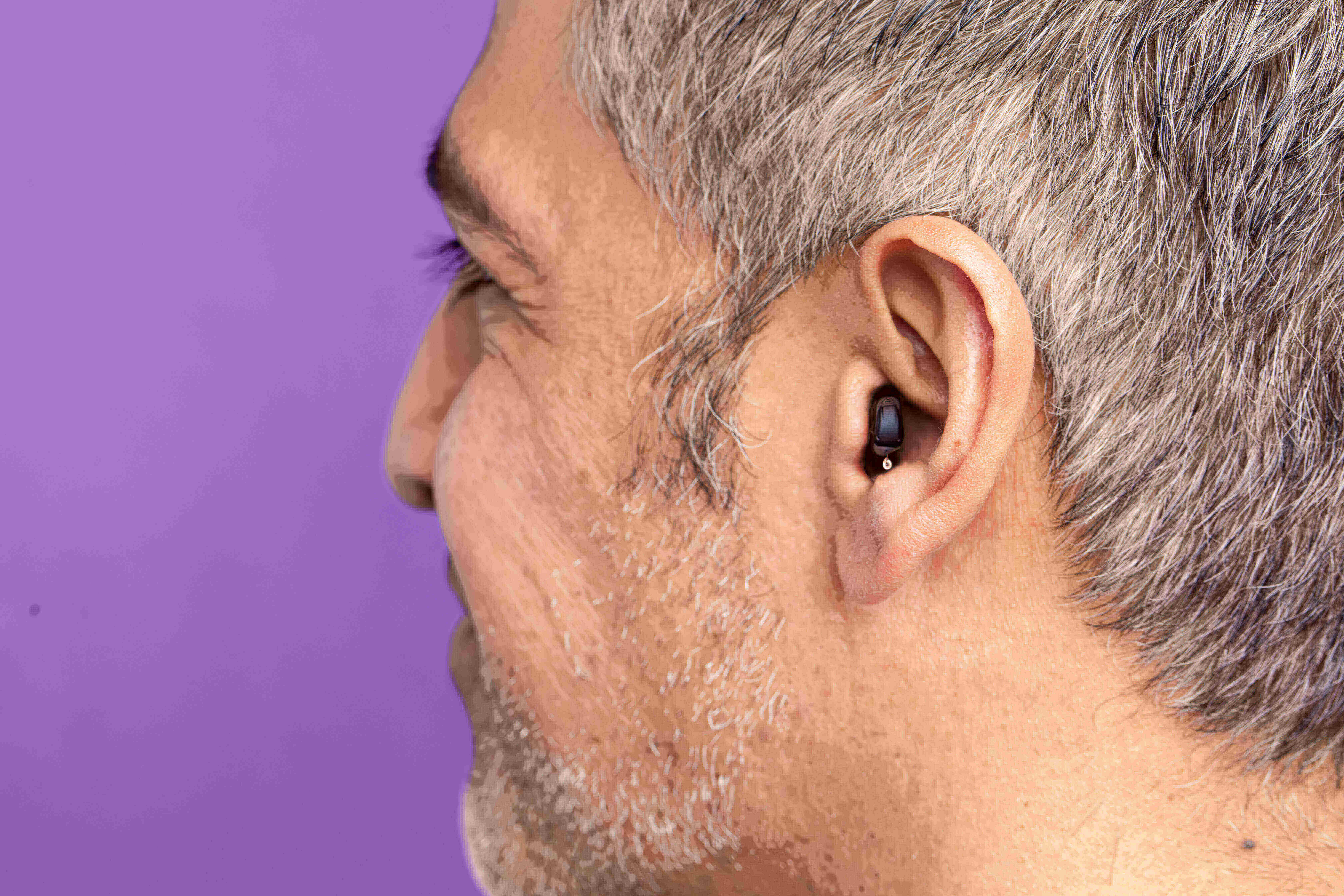 Man with earbud, gray hair, purple background.